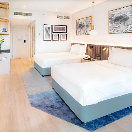 Radisson Blu Hotel & Resort, Abu Dhabi Corniche Esterno foto The image shows a modern hotel room featuring two double beds with white linens. The room has a light and airy ambiance, with wooden flooring and a complementary area rug. There are decorative wall frames with artwork above the beds, and a stylish pe