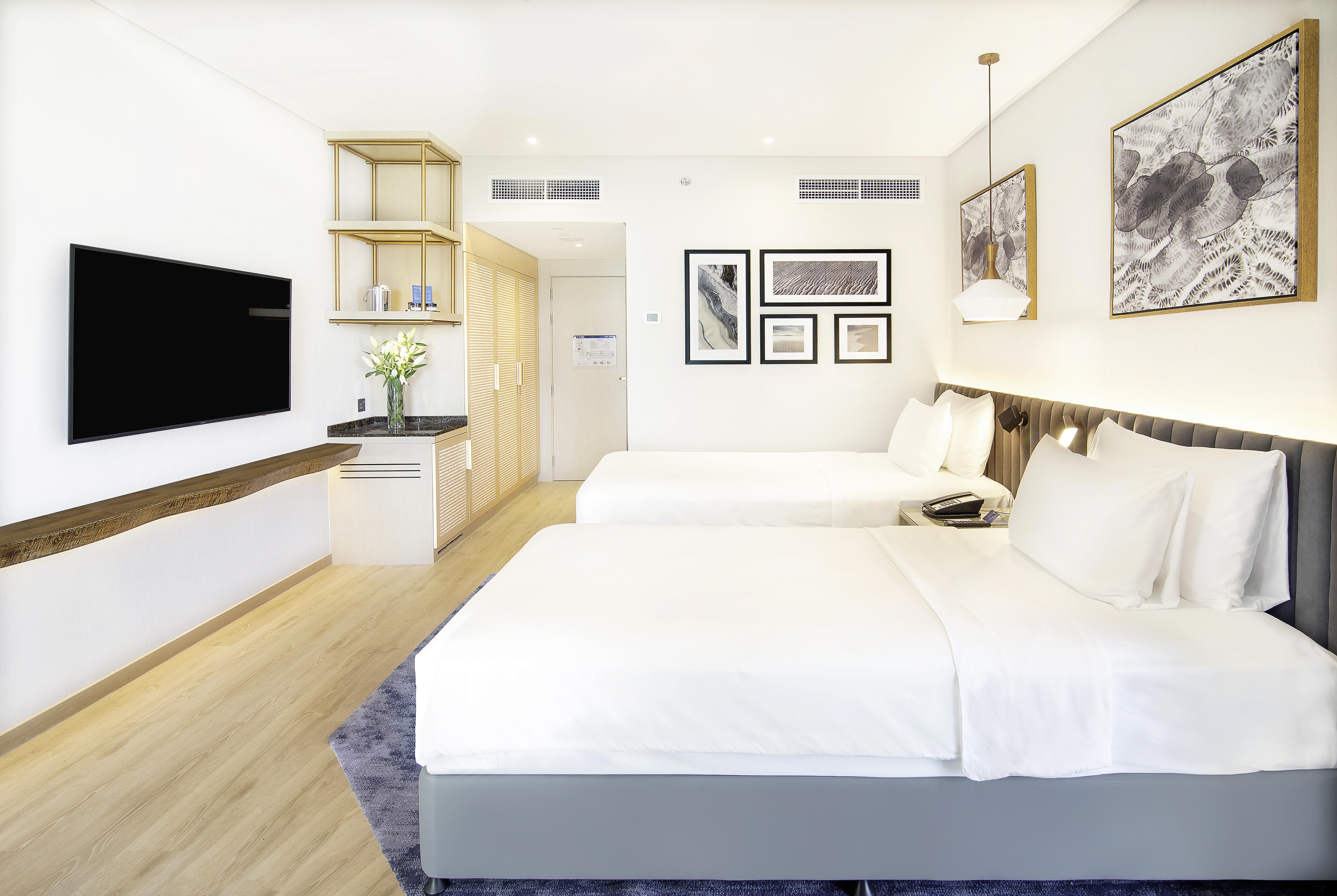 Radisson Blu Hotel & Resort, Abu Dhabi Corniche Esterno foto The photo shows a modern hotel room featuring two double beds with white bedding. The room has a clean and minimalist design, with light wooden flooring and soft, neutral colors. A flat-screen TV is mounted on the wall across from the beds. There's a
