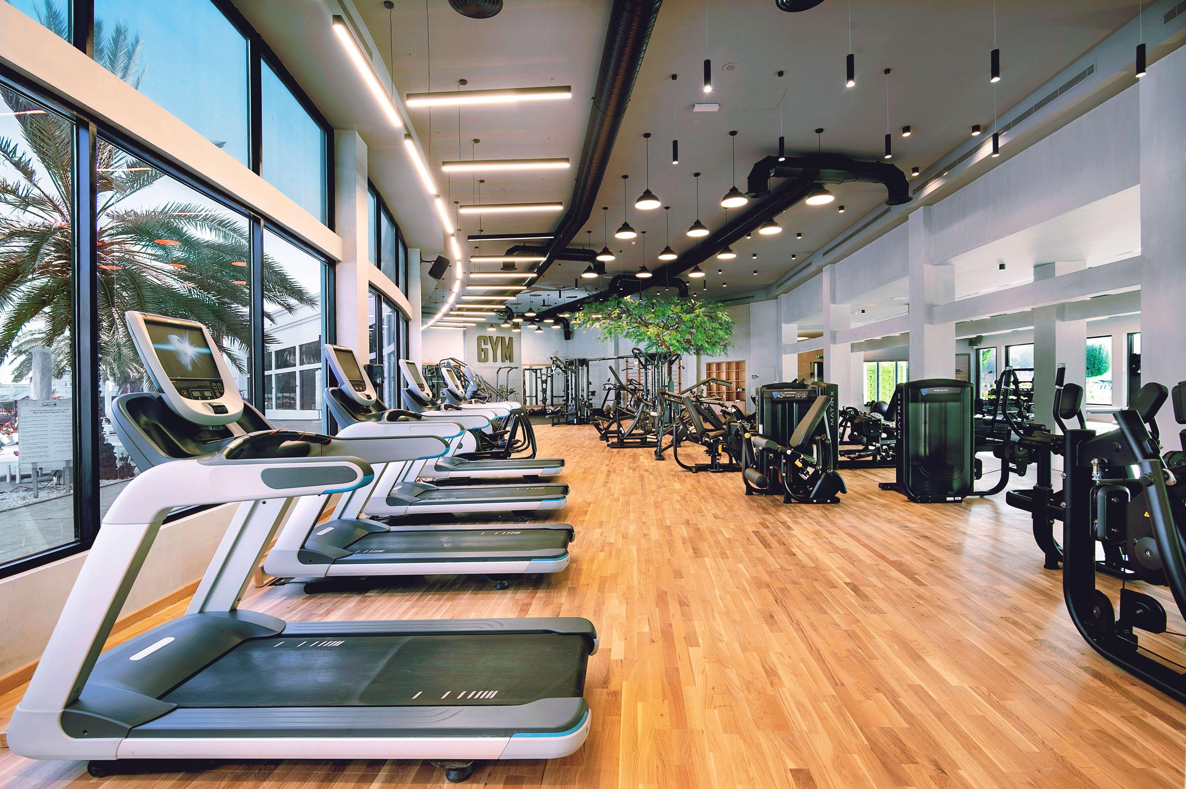Radisson Blu Hotel & Resort, Abu Dhabi Corniche Esterno foto The photo shows a modern gym interior with numerous exercise machines. In the foreground, there are several treadmills positioned side by side on a wooden floor. The gym features large windows that let in natural light and provide a view of greenery 