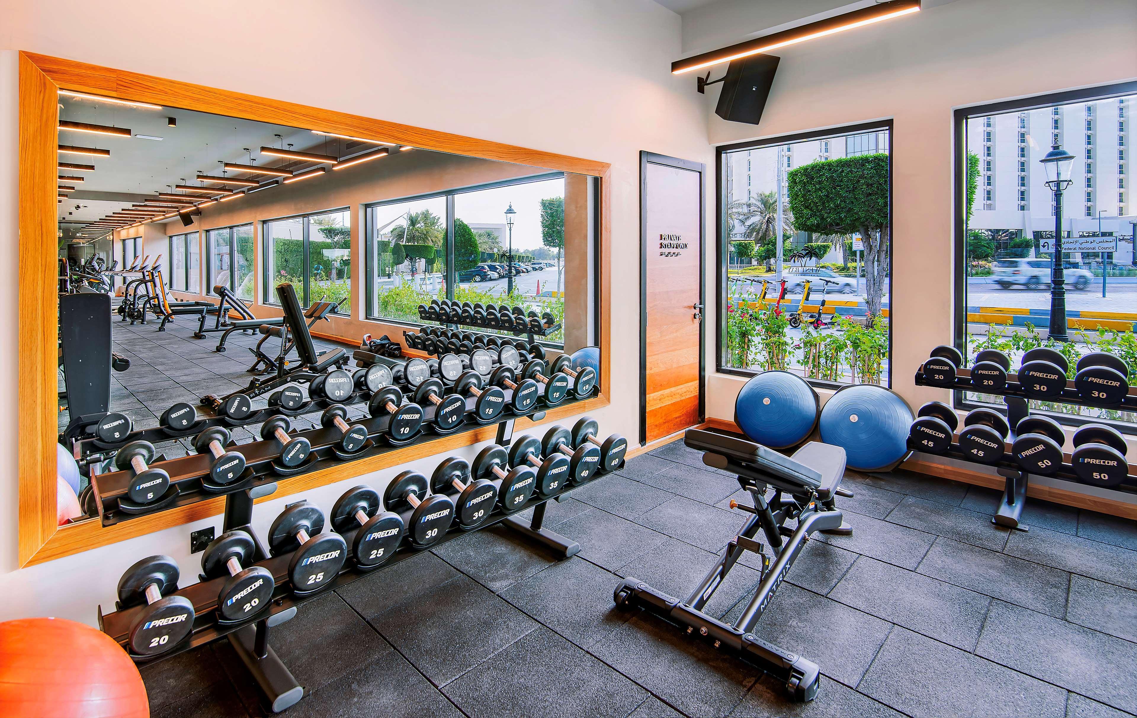 Radisson Blu Hotel & Resort, Abu Dhabi Corniche Esterno foto The photo shows a modern gym interior featuring various workout equipment. On one side, there is a row of dumbbells neatly arranged on a rack. In the center, a workout bench is positioned, likely for strength training exercises. There are also exerci