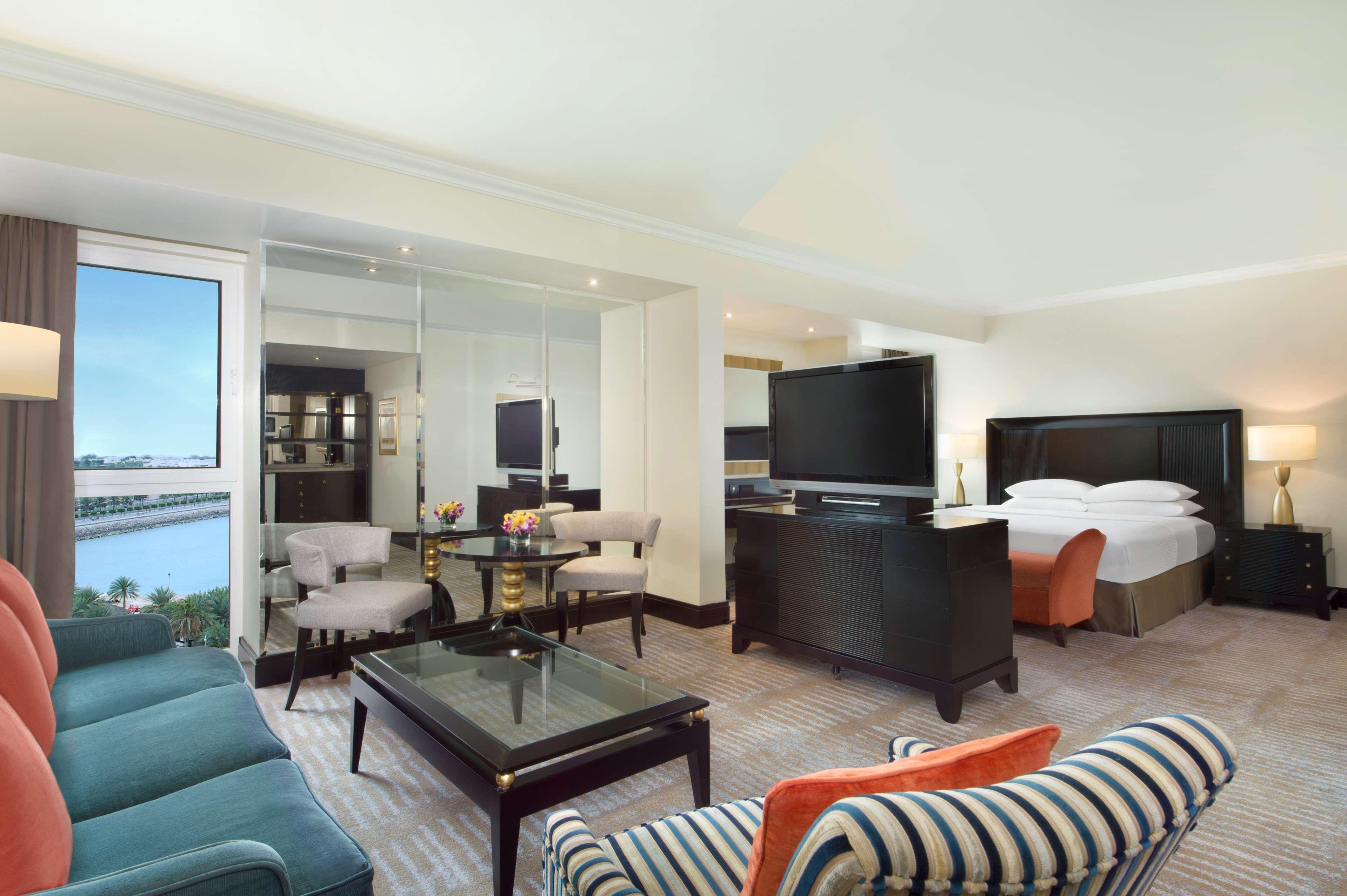 Radisson Blu Hotel & Resort, Abu Dhabi Corniche Esterno foto The photo depicts a spacious hotel suite. The room features a comfortable seating area with a blue couch and striped armchairs. There's a coffee table in the center, and a flat-screen television is mounted on a dark wooden cabinet. In the background,