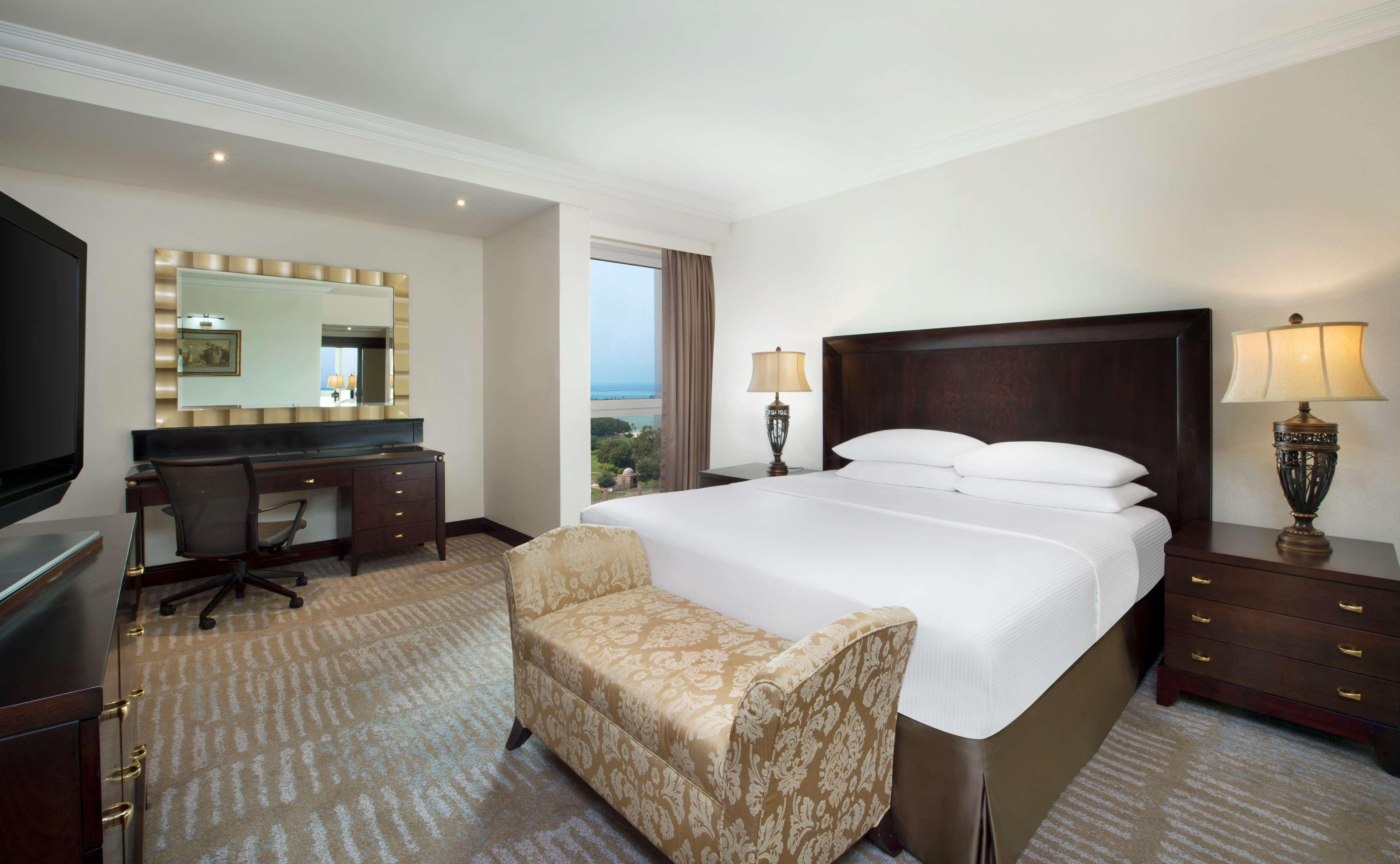 Radisson Blu Hotel & Resort, Abu Dhabi Corniche Esterno foto The photo shows a well-decorated hotel room featuring a comfortable king-sized bed with crisp white linens. There’s a stylish armchair at the foot of the bed. To one side, there's a desk with a chair, providing a workspace. A large mirror with a deco