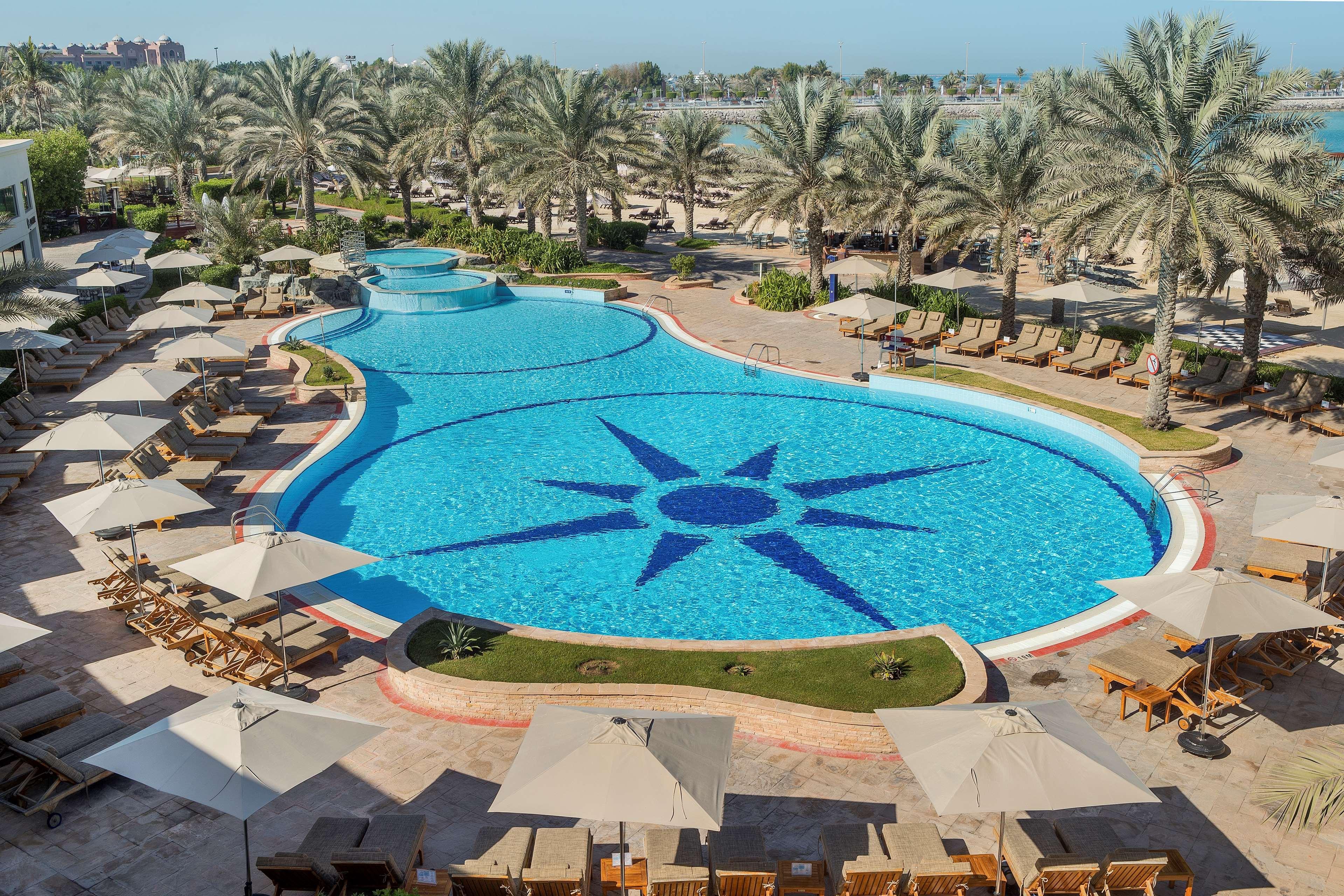 Radisson Blu Hotel & Resort, Abu Dhabi Corniche Esterno foto The image depicts a large, beautifully designed swimming pool shaped like a freeform design, featuring a prominent star pattern at its center. Surrounding the pool are numerous lounge chairs with light-colored cushions and umbrellas, providing shade.