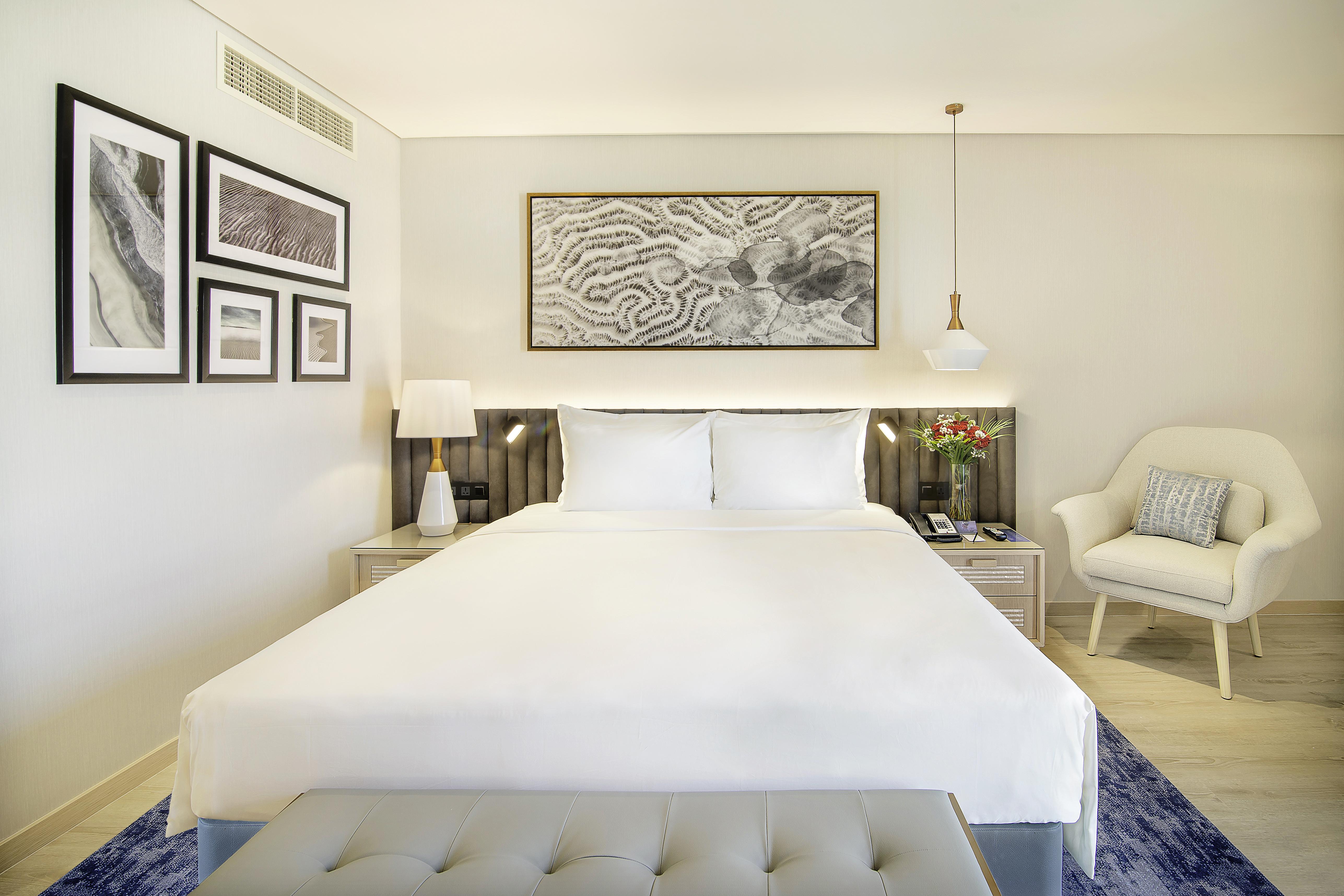 Radisson Blu Hotel & Resort, Abu Dhabi Corniche Esterno foto The photo shows a well-decorated hotel room featuring a king-sized bed with crisp white linens. There are two bedside tables, each with a lamp, on either side of the bed. Above the bed is a large framed artwork, adding a touch of elegance to the spac