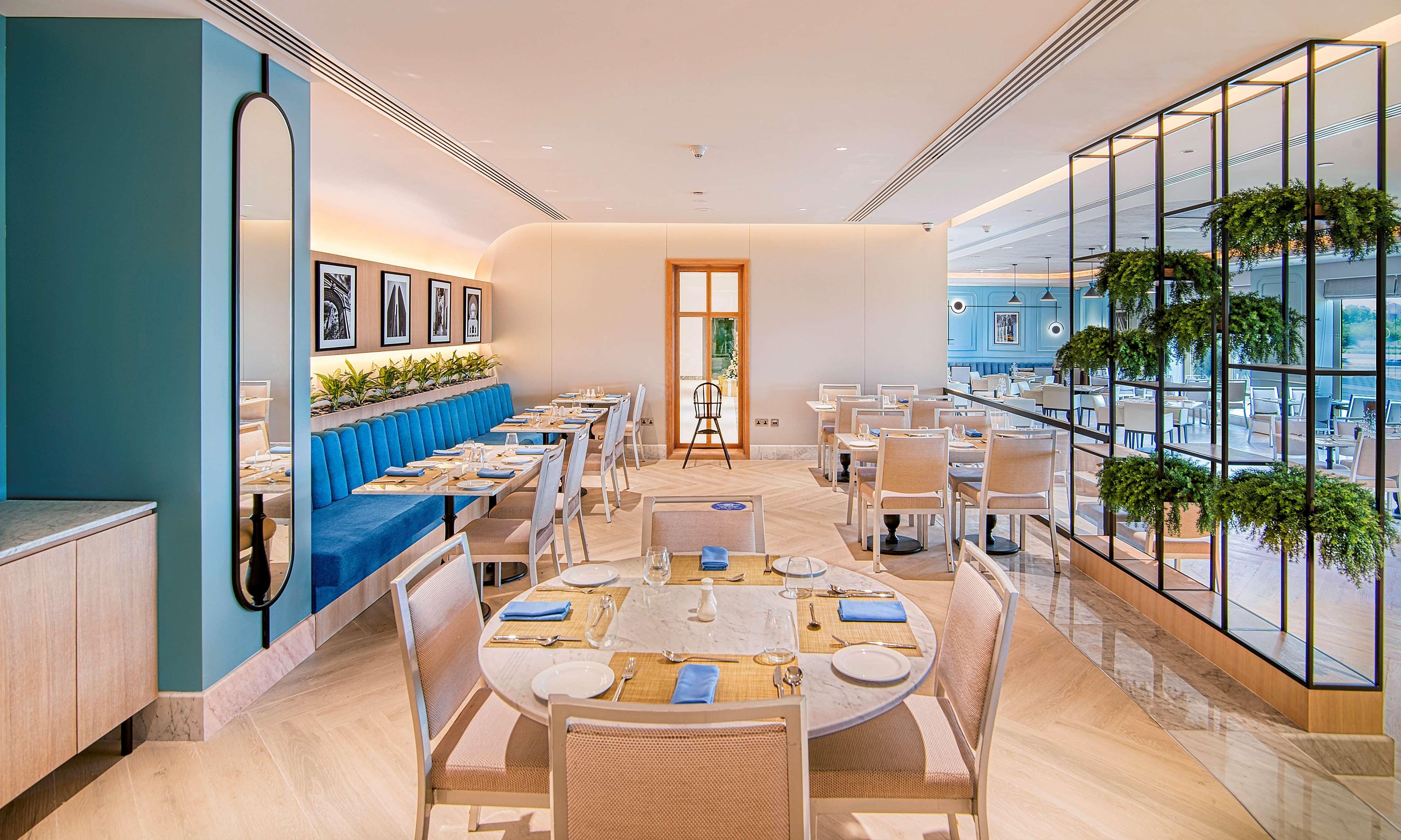 Radisson Blu Hotel & Resort, Abu Dhabi Corniche Esterno foto The photo showcases a modern restaurant interior. It features a mix of light and vibrant colors, with blue upholstered seating along one wall. Tables are elegantly set with blue napkins and white dishware. The space has a bright, airy feel, enhanced 