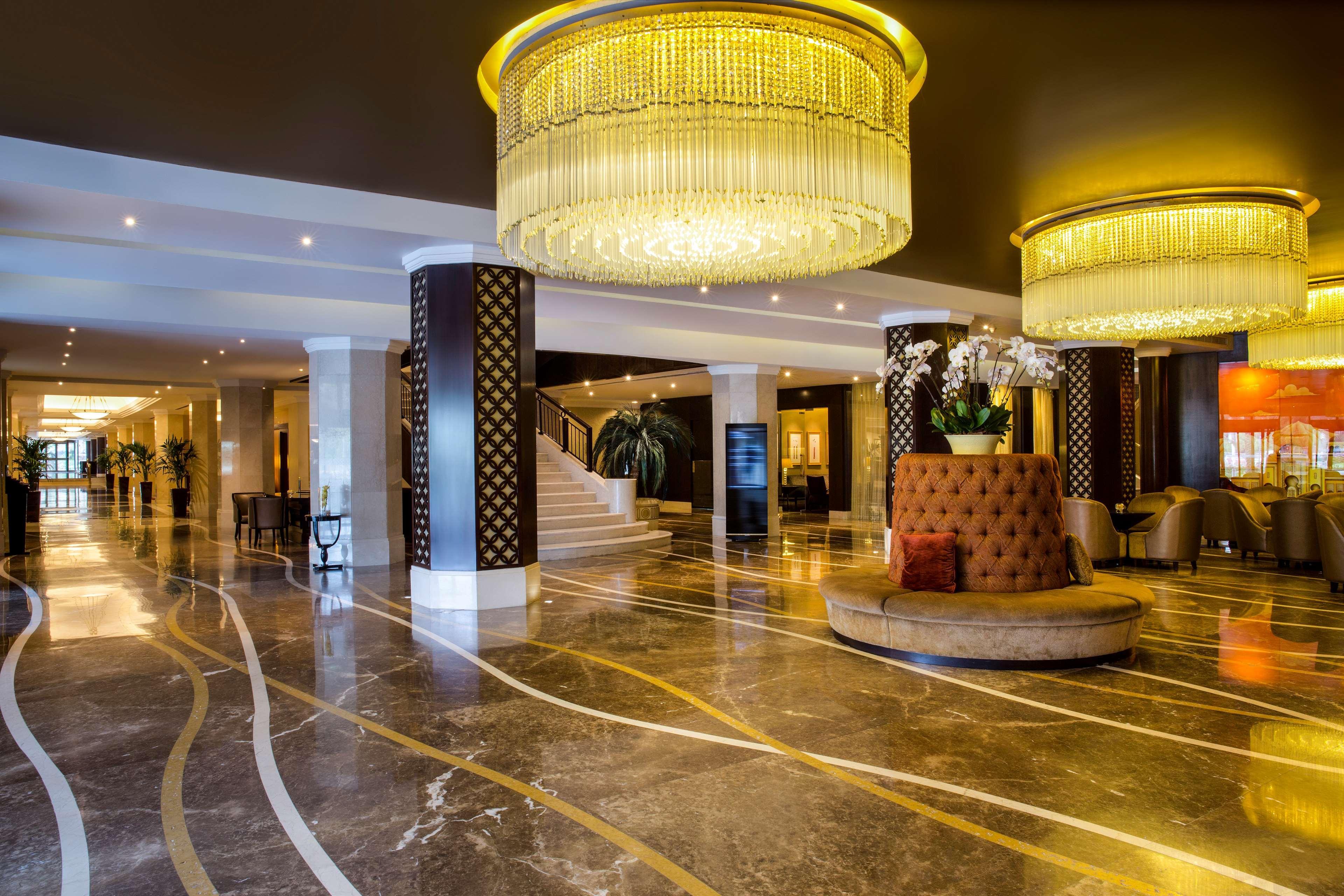 Radisson Blu Hotel & Resort, Abu Dhabi Corniche Esterno foto The photo depicts an elegant hotel lobby with a luxurious ambiance. The flooring is made of polished marble, featuring decorative swirling lines. There are two large, ornate chandeliers hanging from the ceiling, providing warm lighting. Column suppor