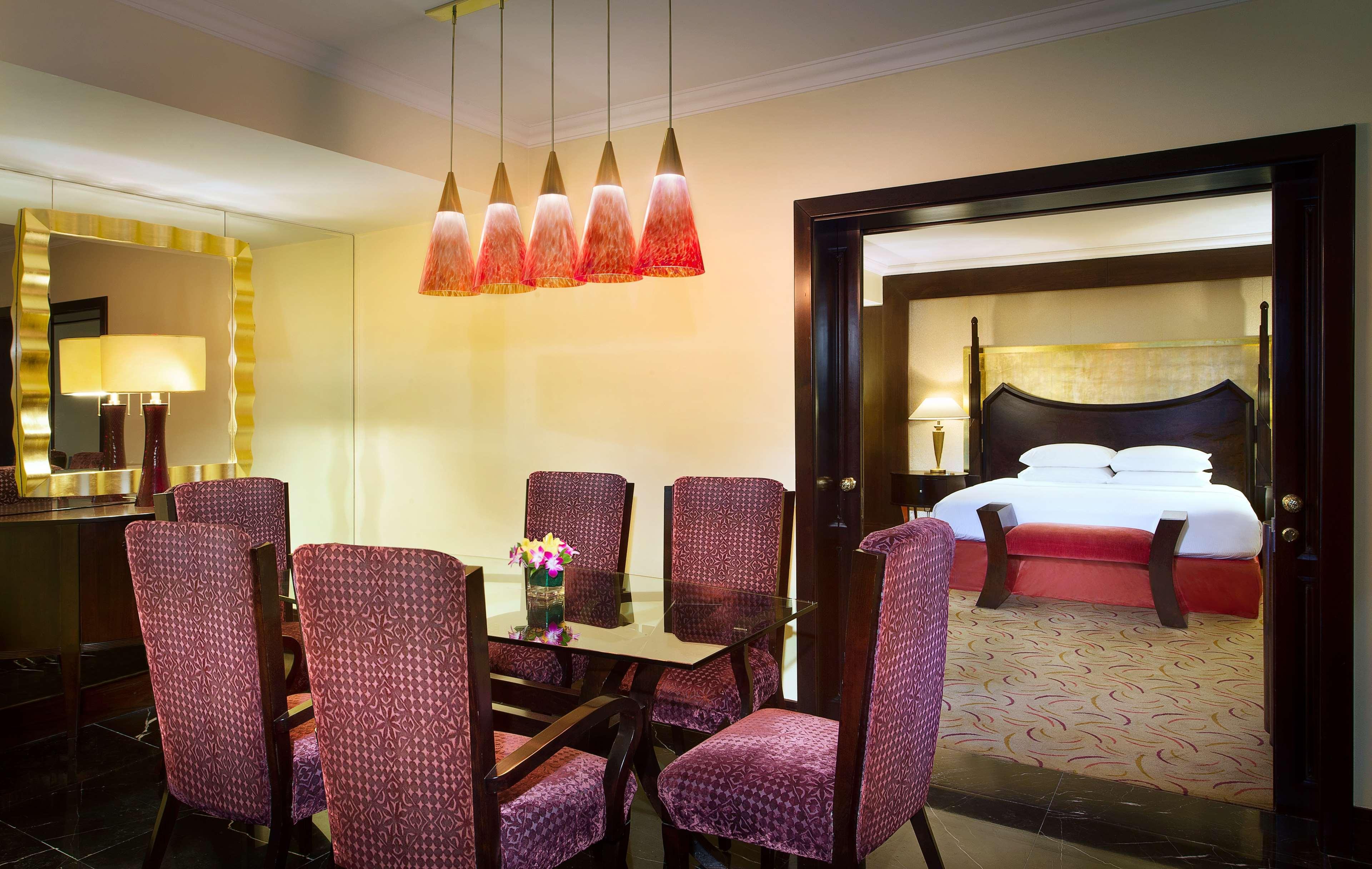 Radisson Blu Hotel & Resort, Abu Dhabi Corniche Esterno foto The photo shows an elegantly decorated room featuring a dining area and a connected bedroom. The dining space has a glass table surrounded by upholstered chairs in a rich, deep color. Above the table, there are multiple pendant lights with a modern d