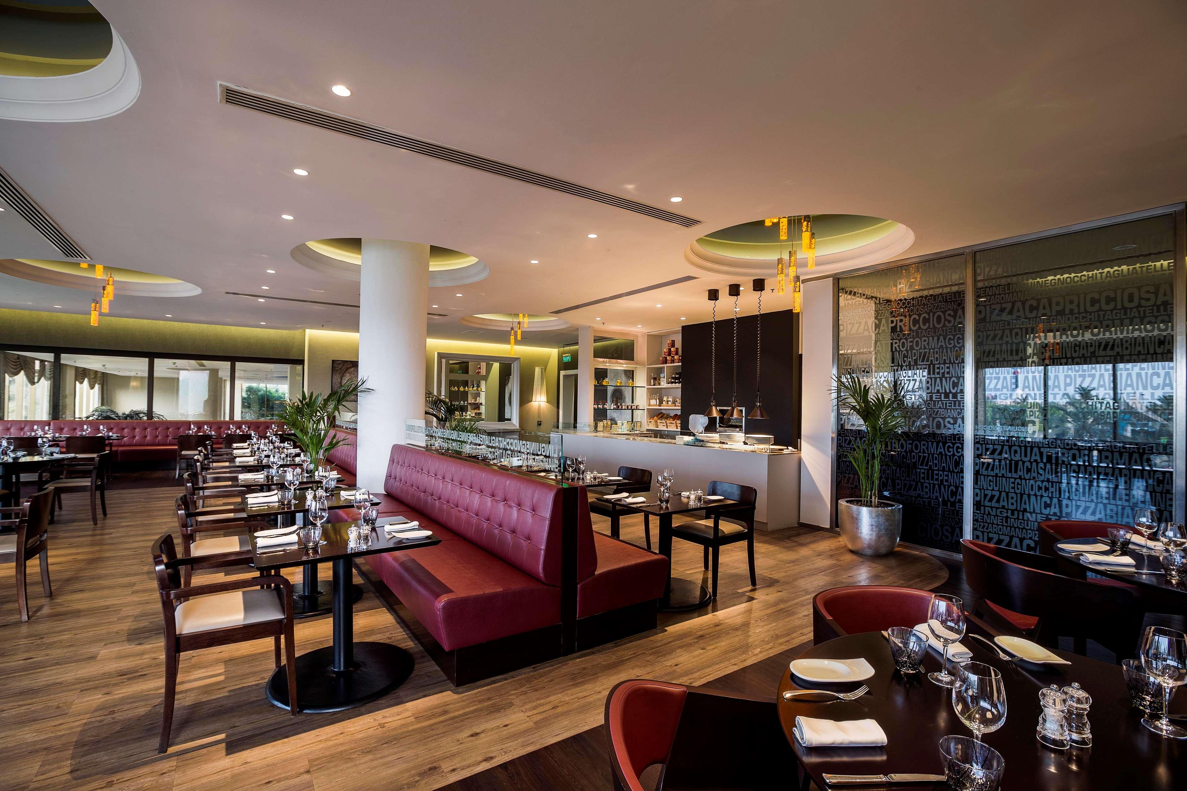 Radisson Blu Hotel & Resort, Abu Dhabi Corniche Esterno foto The photo shows a modern restaurant interior with a stylish design. It features a mix of dark wood and plush upholstery, with booths and tables arranged neatly. The booths are upholstered in a deep red fabric, while the tables are set with cutlery an