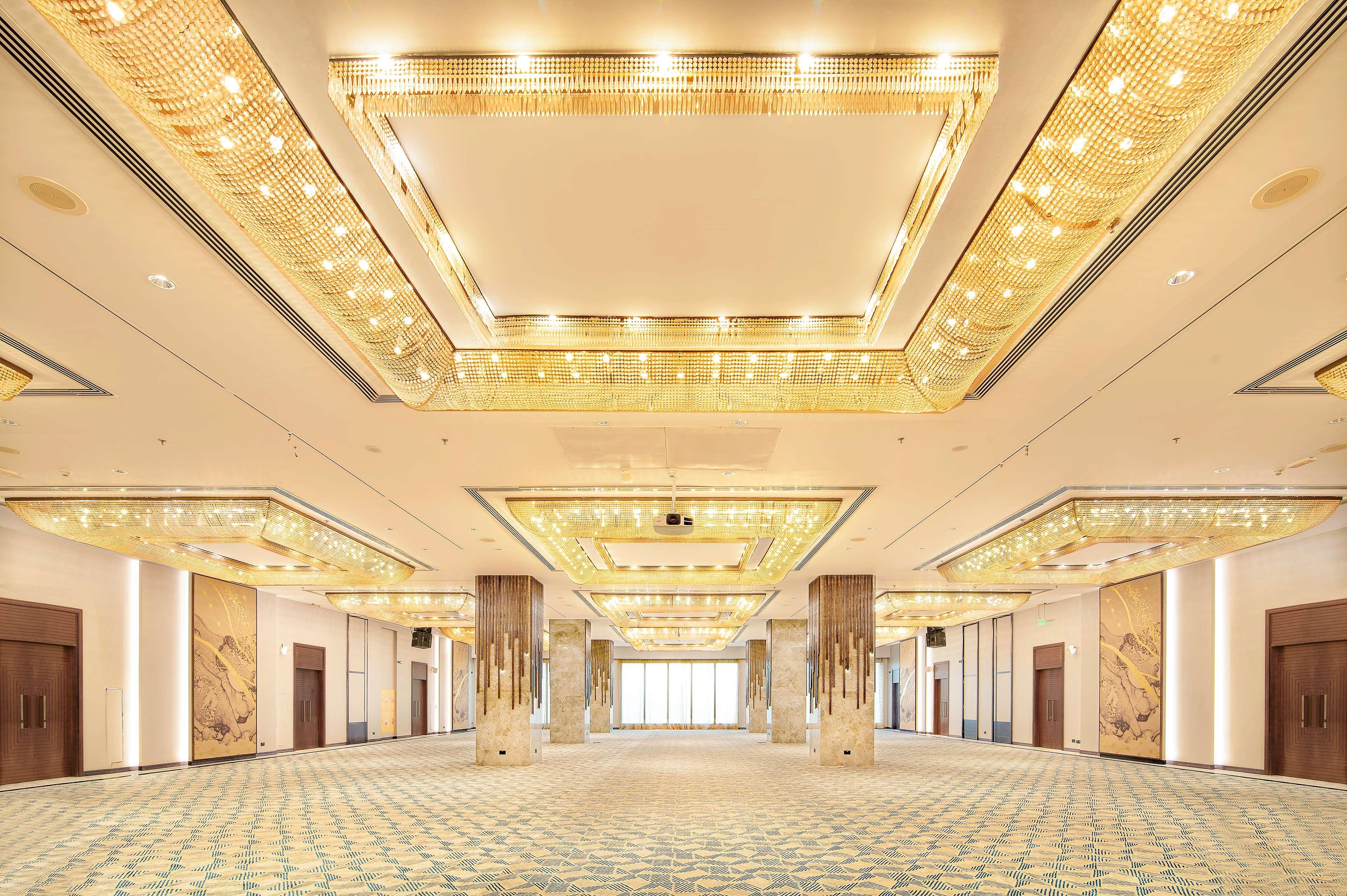 Radisson Blu Hotel & Resort, Abu Dhabi Corniche Esterno foto The photo shows a spacious, elegantly designed interior, likely a banquet or conference hall. The ceiling features a luxurious design with intricate lighting elements that give off a warm glow. The floor is covered with a patterned carpet in soft col