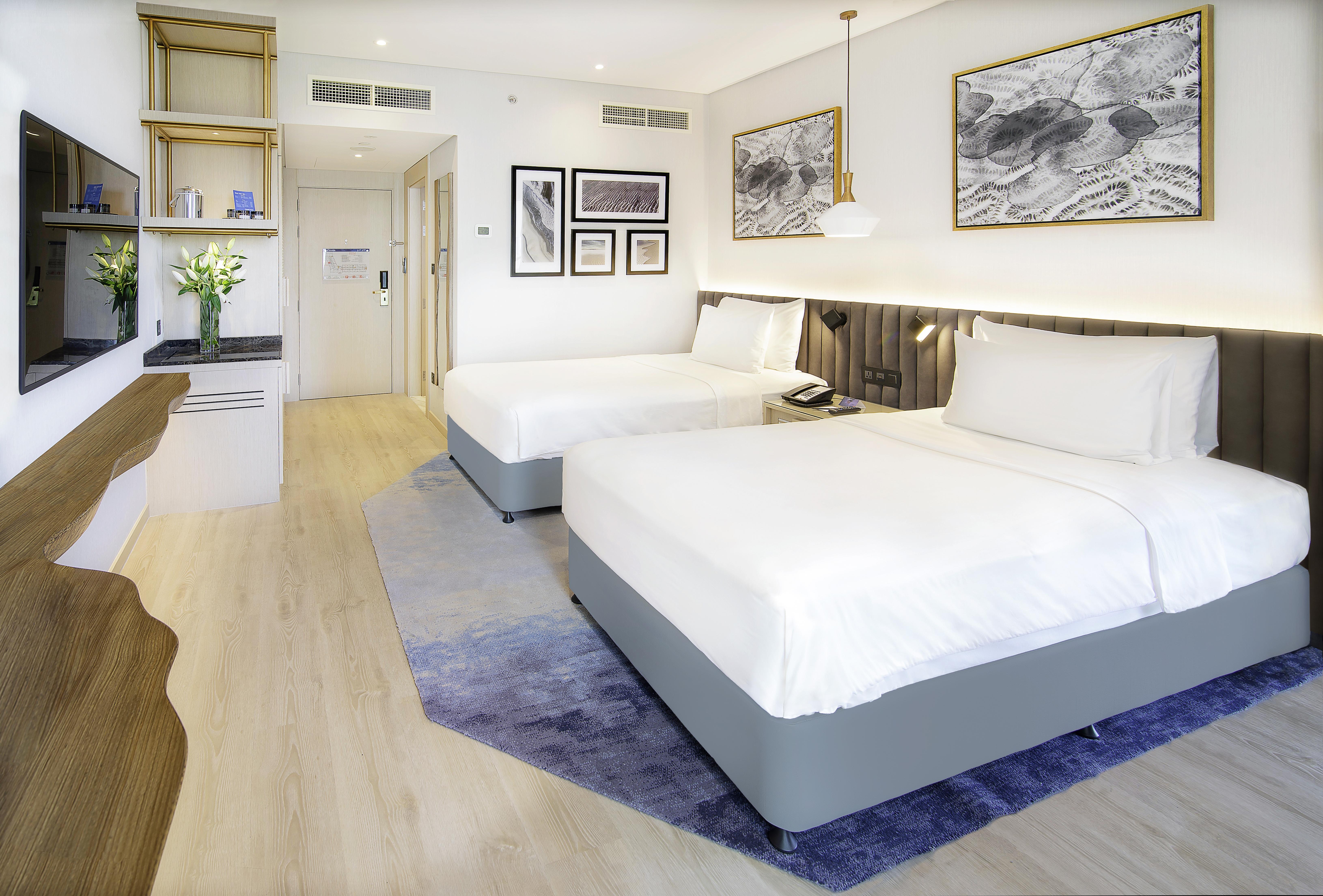 Radisson Blu Hotel & Resort, Abu Dhabi Corniche Esterno foto The image shows a modern hotel room featuring two double beds with white linens. The room has a light and airy ambiance, with wooden flooring and a complementary area rug. There are decorative wall frames with artwork above the beds, and a stylish pe