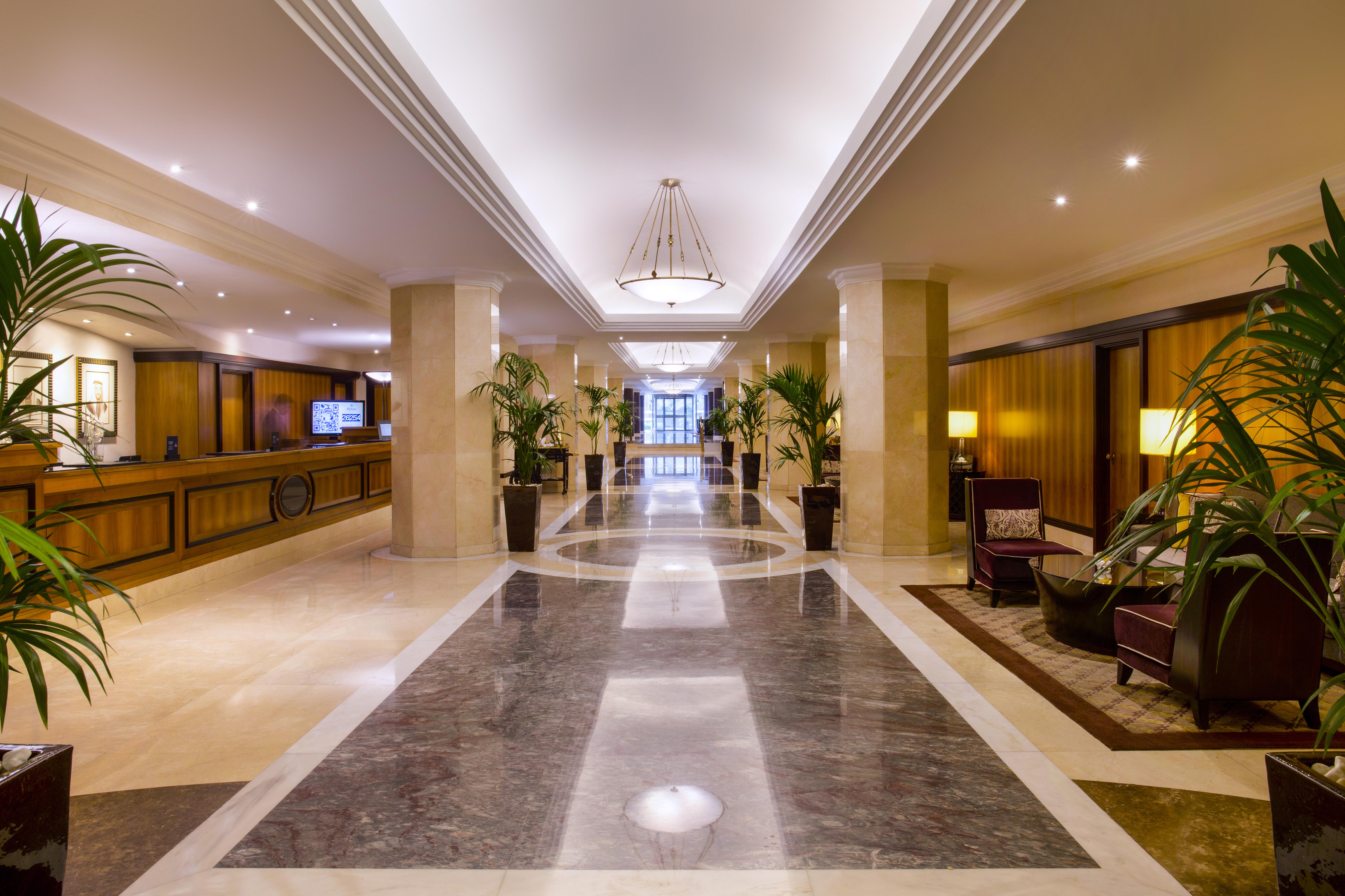 Radisson Blu Hotel & Resort, Abu Dhabi Corniche Esterno foto The photo displays an elegant hotel lobby. It features a spacious hallway with polished marble flooring and decorative lighting. On either side of the corridor are tall potted plants, adding a touch of greenery to the space. The reception desk is vis