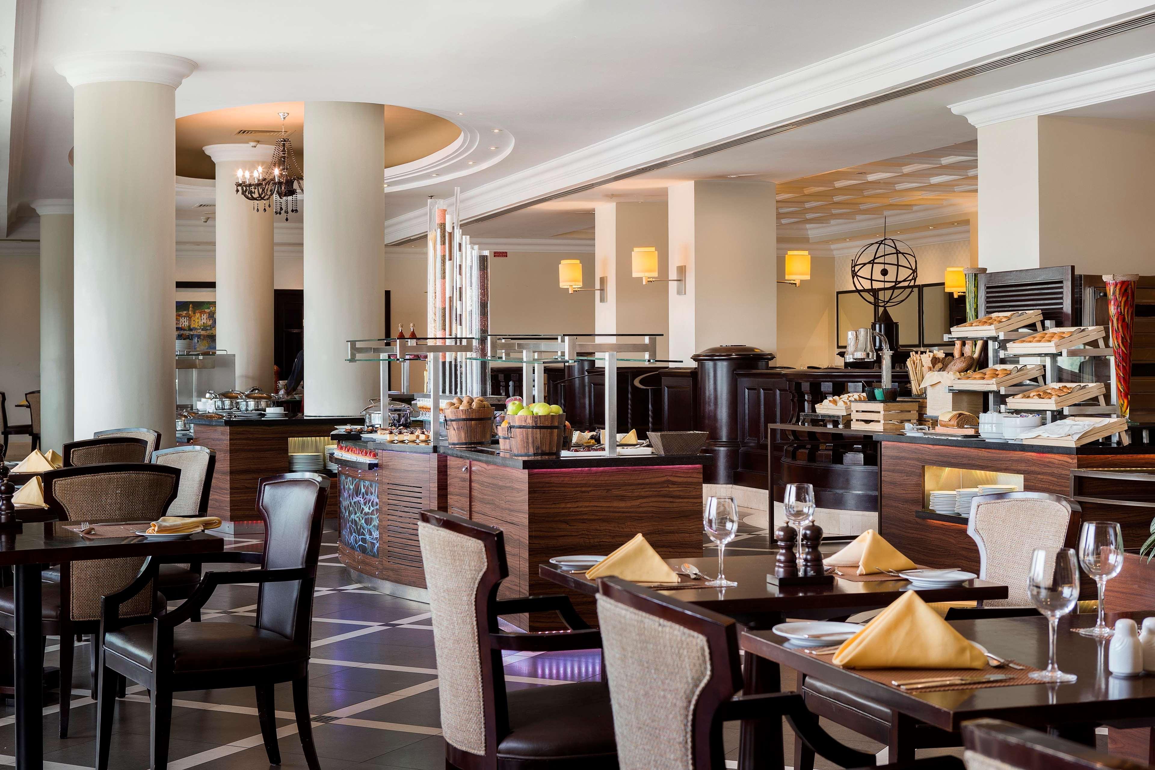 Radisson Blu Hotel & Resort, Abu Dhabi Corniche Esterno foto The photo shows an elegant dining area of a restaurant. There are well-set tables with dark wooden furniture, featuring white tablecloths and neatly folded yellow napkins. The restaurant has a modern decor, with large pillars and ambient lighting fro