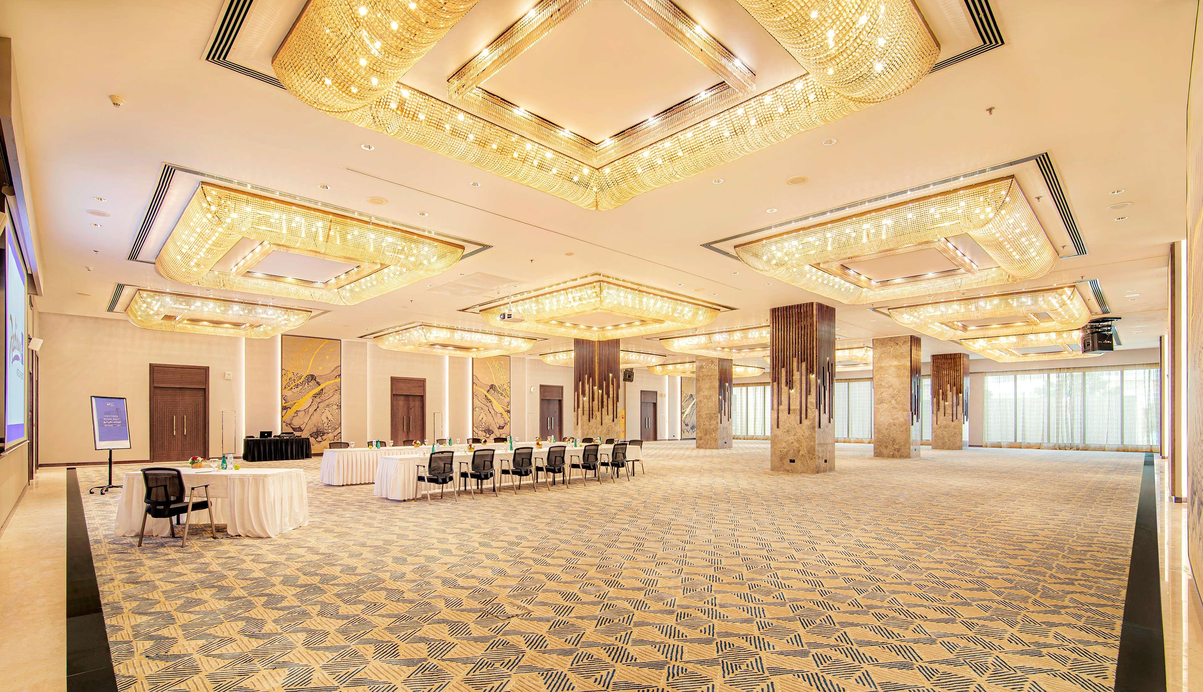 Radisson Blu Hotel & Resort, Abu Dhabi Corniche Esterno foto The photo shows an elegant event space or banquet hall with a spacious layout. The ceiling features intricate designs and is adorned with multiple chandeliers that provide ample lighting. The floor has an artistic carpet pattern. To one side, there a