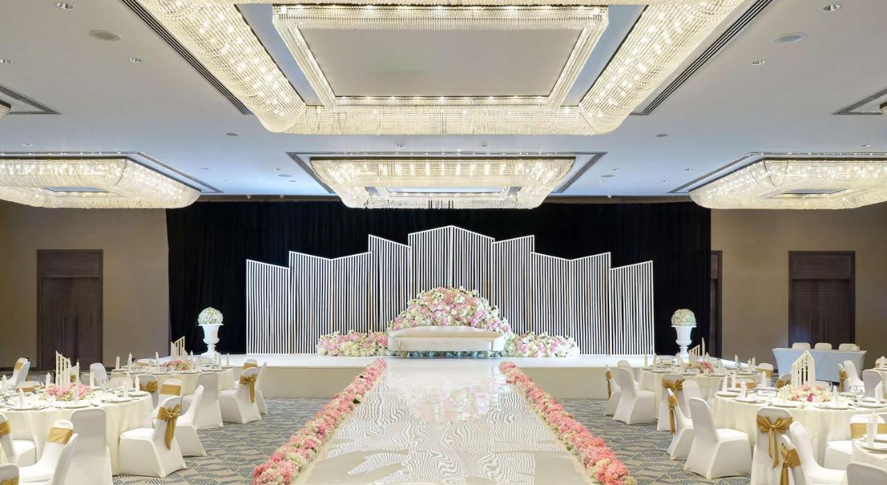 Radisson Blu Hotel & Resort, Abu Dhabi Corniche Esterno foto The photo depicts a beautifully arranged wedding or event venue. In the center, there is a stage adorned with decorative elements, including a backdrop made of white and silver panels and a floral arrangement featuring pastel-colored flowers. The ais