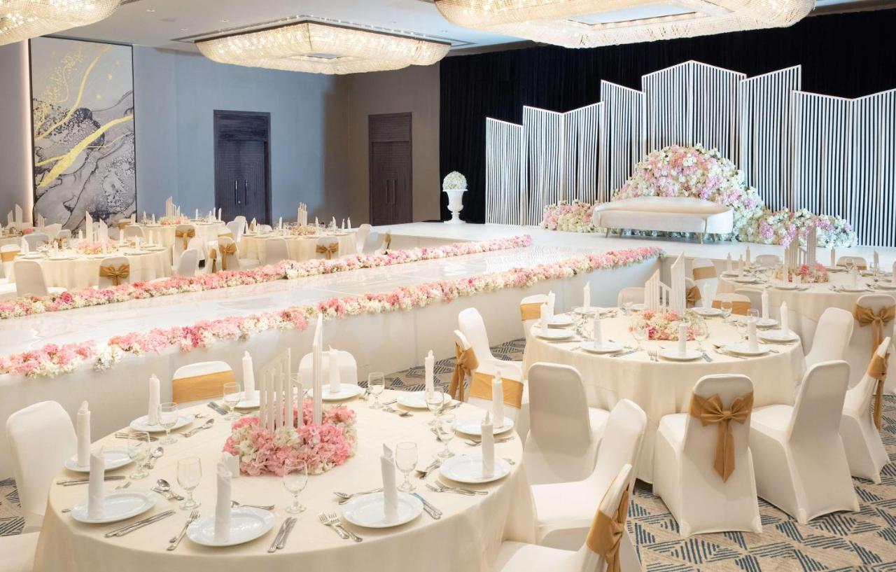 Radisson Blu Hotel & Resort, Abu Dhabi Corniche Esterno foto The photo shows a beautifully arranged banquet setting. There are round tables with white tablecloths, each adorned with elegant table settings, including plates and candles. The centerpiece of the room features a long table decorated with floral arr
