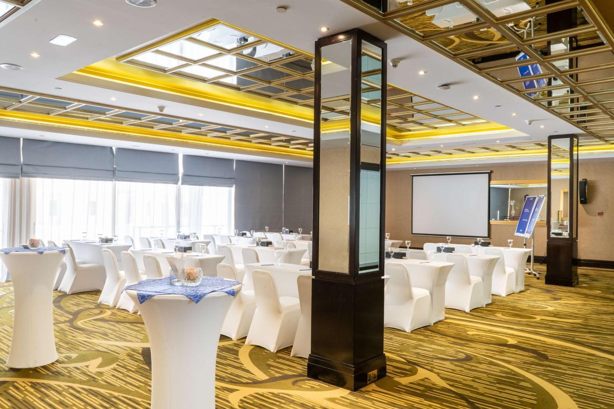 Radisson Blu Hotel & Resort, Abu Dhabi Corniche Esterno foto The photo depicts a modern event or conference room set up for a gathering. The space features several tables covered with white tablecloths, arranged for attendees. The room is well-lit with a combination of natural light from large windows and arti