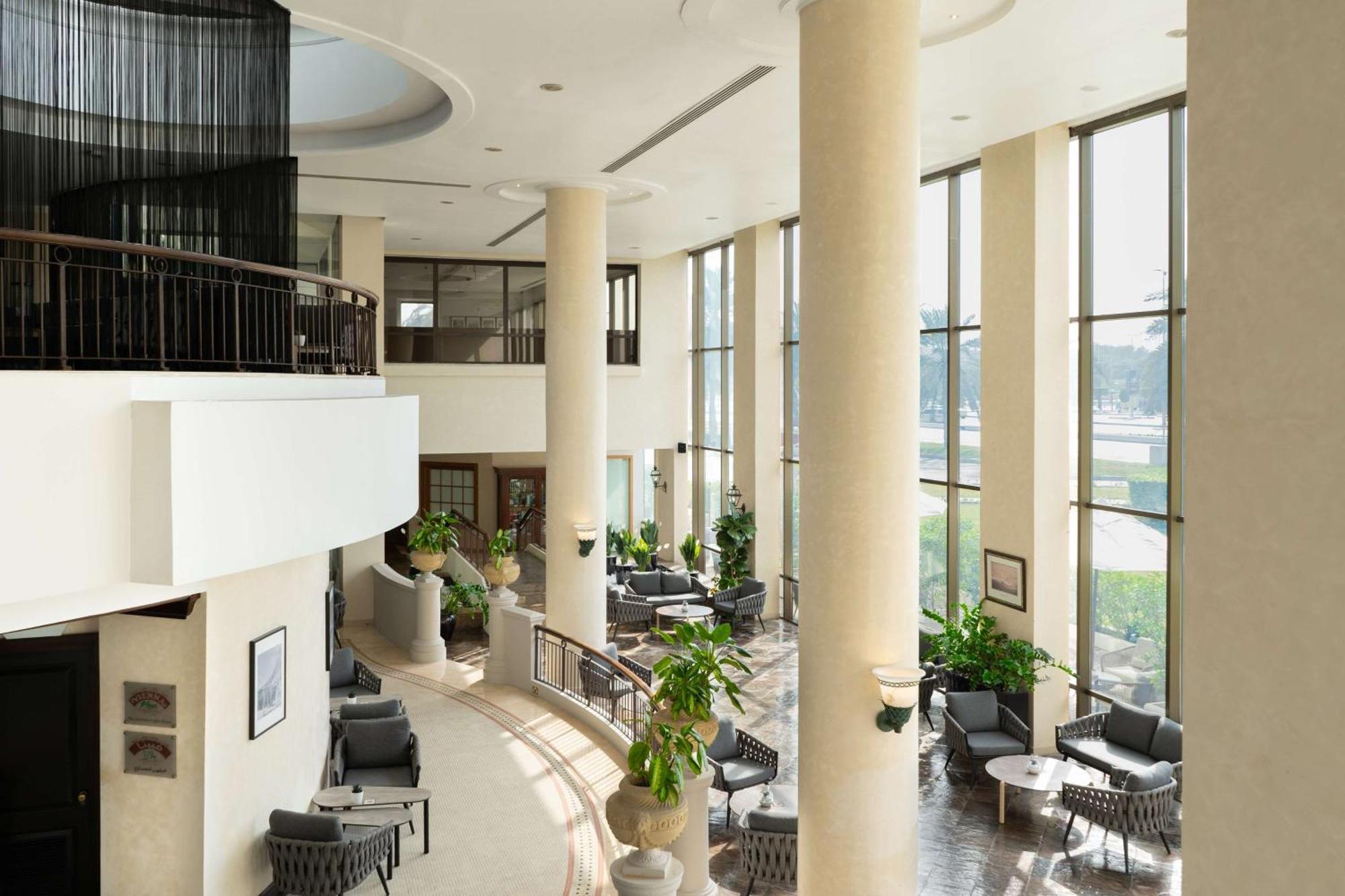 Radisson Blu Hotel & Resort, Abu Dhabi Corniche Esterno foto The photo shows a spacious, well-lit interior area, likely a lobby or common space in a building. There are tall columns and large windows that let in natural light, creating an airy atmosphere. Comfortable seating arrangements with chairs and small 
