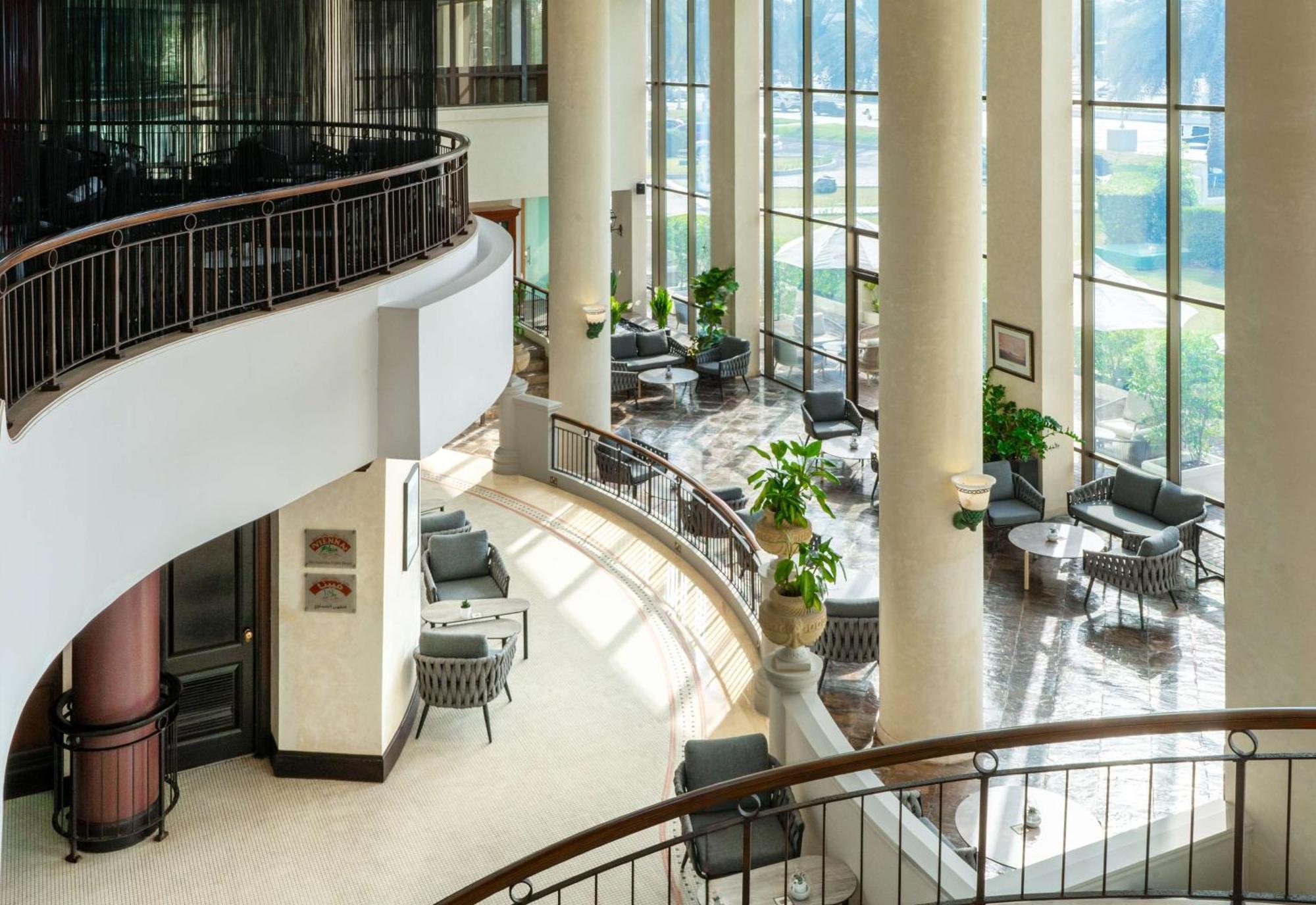 Radisson Blu Hotel & Resort, Abu Dhabi Corniche Esterno foto The photo depicts a modern interior space, likely within a hotel or a commercial building. It features large windows that allow natural light to flood in, creating a bright and inviting atmosphere. The design includes tall columns and a curved balcon