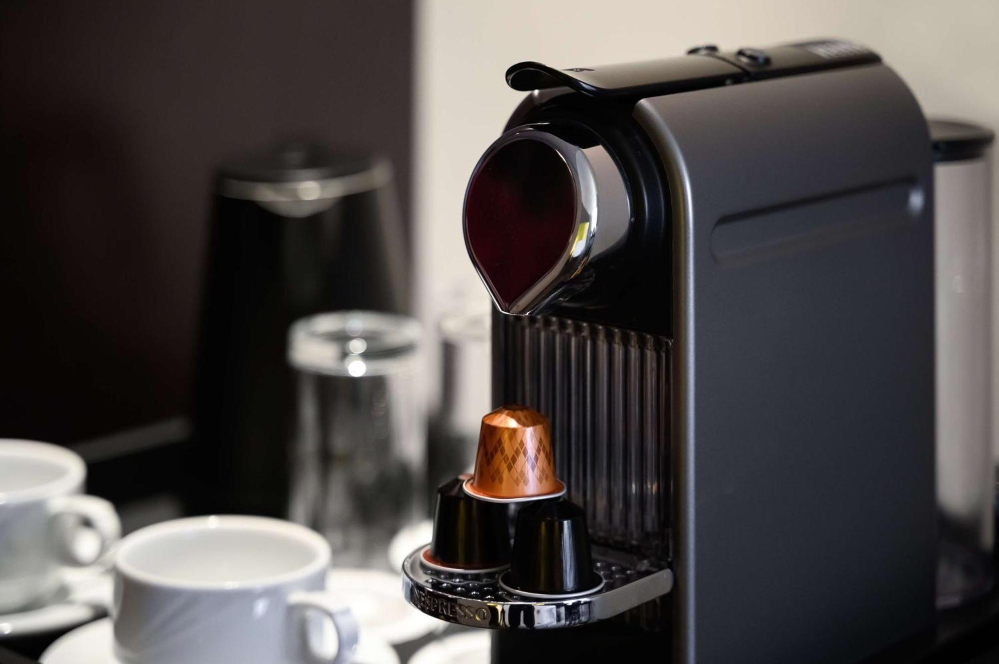 Radisson Blu Hotel & Resort, Abu Dhabi Corniche Esterno foto The photo shows a sleek, modern coffee machine, likely a Nespresso model, in the process of brewing coffee. The machine is primarily black with a shiny finish. There is a cup placed underneath the spout, which is dispensing a stream of dark coffee. N
